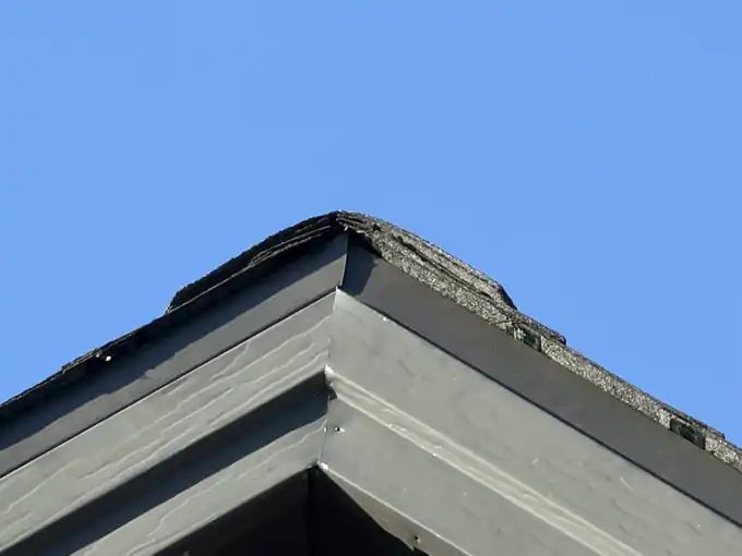 Gable ridge against blue sky with a worn and damaged ridge cap