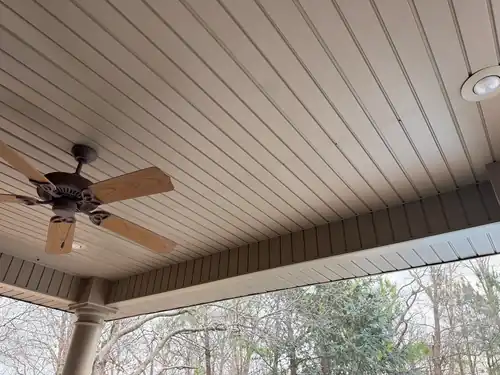 New soffit panels under a porch overhang with a fan and trees beyond