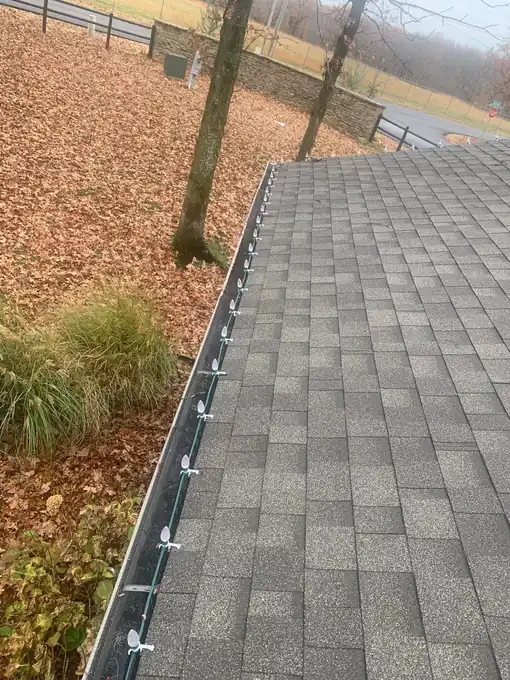 New seamless gutter with hidden hangers along a shingle roof edge in autumn leaves