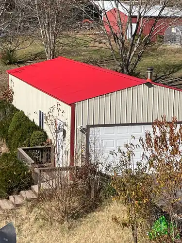 Bright red new metal roof on a cream steel shop building with a garage door in Springdale