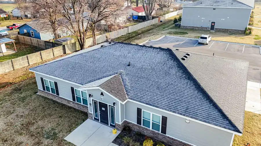Drone view of a single-storey apartment building in Siloam Springs with a new dark shingle roof and a parking lot behind