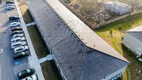 Drone view down a long apartment ridge line beside a full parking lot