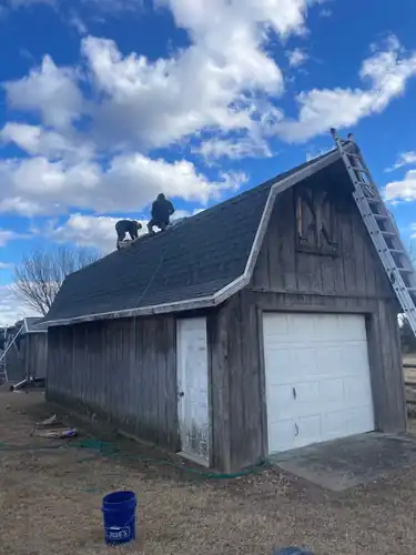 Weathered-wood gambrel barn with a new dark shingle roof and a ladder up to the crew