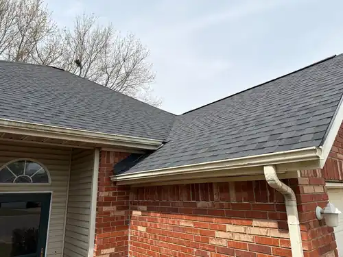 Corner of a brick Springdale home with new CertainTeed Landmark Moire Black shingles, gutter and downspout